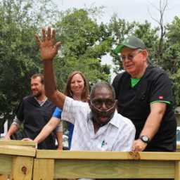 Claude Adams waves to neighbors as Ken Whitaker of Legend Healthcare helps him up his new ramp. Kelly Wickersham, OTA of Legend, and April Wilson, RN, BSN, of CIMA Hospice, celebrate his homecoming Sunday.